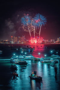 Firework display over sea in city against sky at night