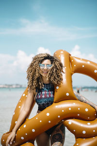 Portrait of smiling woman holding pool raft while standing at beach