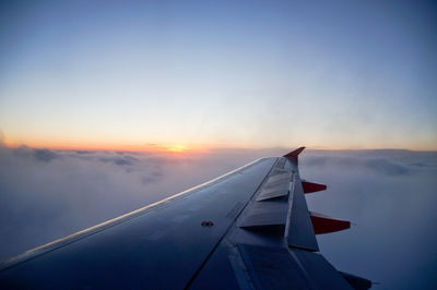 Cropped image of airplane flying over clouds during sunset