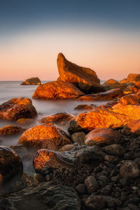 Rocks on sea shore against sky during sunset