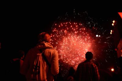 Rear view of people enjoying firework display at night