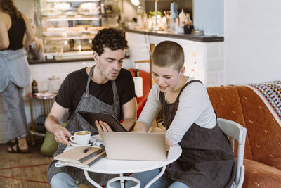 Male and female colleagues discussing over laptop while sitting on chair in cafe