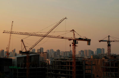 Cranes in city against sky during sunset