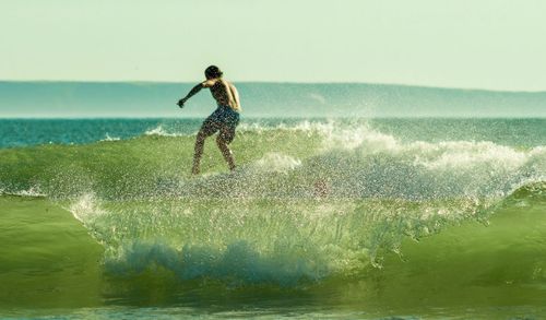 Rear view of man surfing on wave in sea against sky