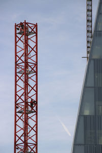 Low angle view of crane by building against sky