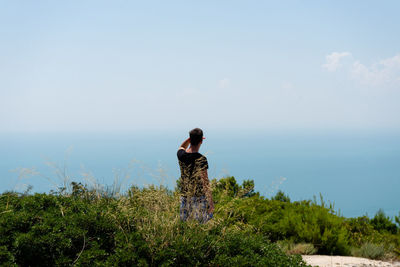 Rear view of man looking at sea while standing amidst plants against sky