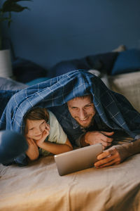 Happy father and son watching a movie on tablet under blanket