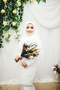 Woman holding flower bouquet against white wall