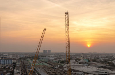 Cranes and buildings against sky during sunset