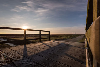 Footpath by railing against sky during sunset