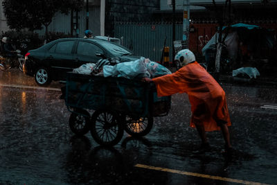 Man pushing cart on wet street during rainy season at night