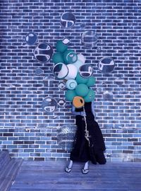 Woman covering face with balloons while standing against brick wall