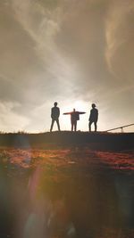 Low angle view of silhouette friends standing on hill against sky