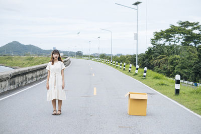 Portrait of young woman standing on road against trees