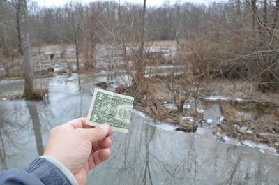 Cropped image of person holding ice cream against trees during winter