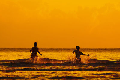 Silhouette man standing on shore against orange sunset sky