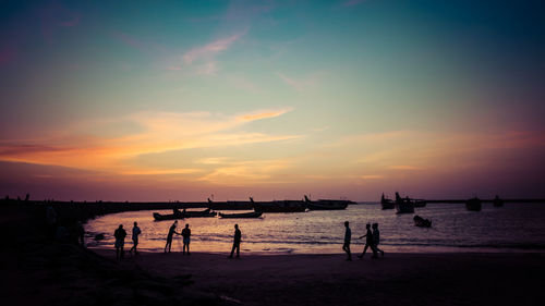 Silhouette people at beach against sky during sunset