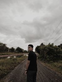 Young man standing on road against sky