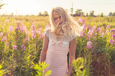 Portrait of teenage girl standing amidst flowering plants on field