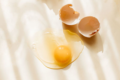 Broken and cracked brown chicken eggshell and raw egg on pastel yellow background