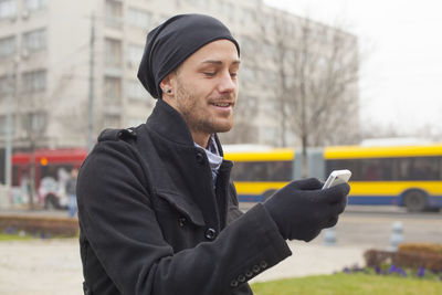 Young man looking away while standing in city during winter