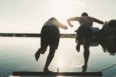 Rear view of friends diving in lake from boat against sky on sunny day