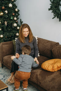 Mother with child playing near christmas tree. child unpacking gifts, woman enjoy christmas tree