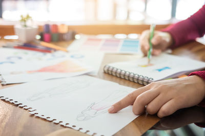 Cropped hand of fashion designer sketching on spiral notebook in office