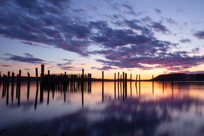 Wooden posts in sea against sky at sunset