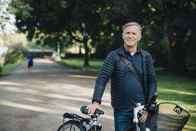 Portrait of smiling senior man with bicycle standing in park