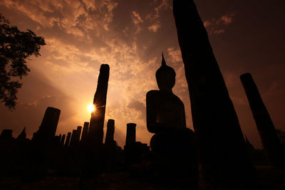 Low angle view of buddha statue against sunset sky
