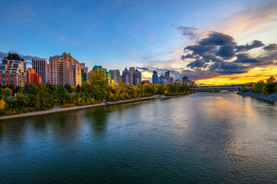 River amidst buildings in city against sky at sunset