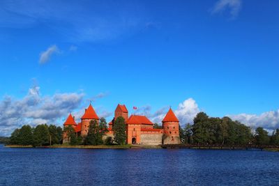 Buildings by river against blue sky