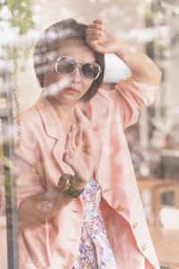 Woman wearing sunglasses seen through window