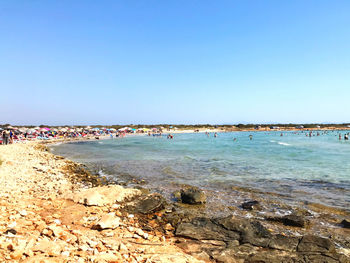 Group of people on beach against clear blue sky