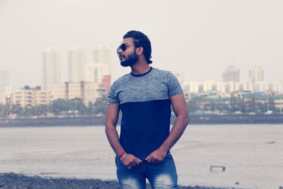 Young man looking away in city against sky