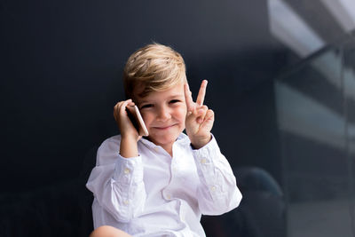 Portrait of cute boy talking on the phone while gesturing peace sign.