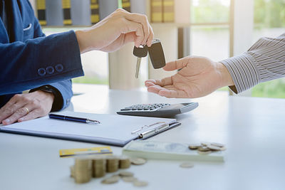 Cropped hand of businessman giving car keys to man on table