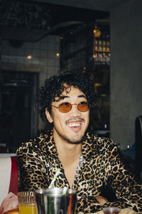 Smiling man with sunglasses looking away while sitting in restaurant during social gathering