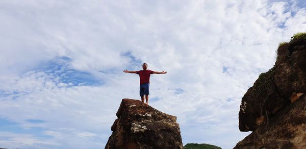 Low angle view of man standing on rock against sky
