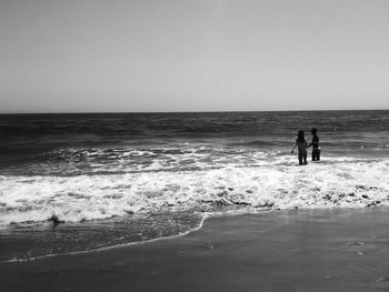 People standing on beach against clear sky