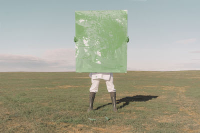 Young woman hiding behind green painting on dry field