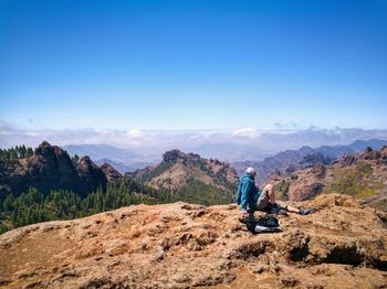 Rear view of man standing on mountain against blue sky