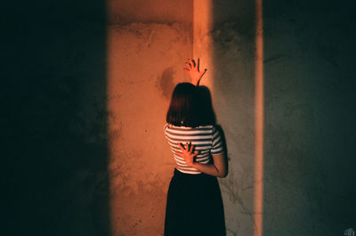 Rear view of woman standing against wall at home