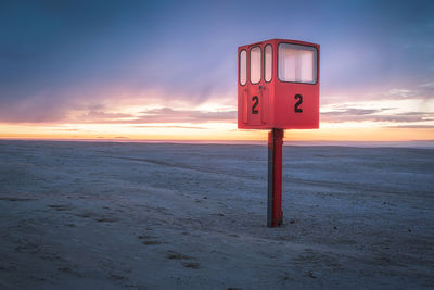 Information sign on beach against sky during sunset