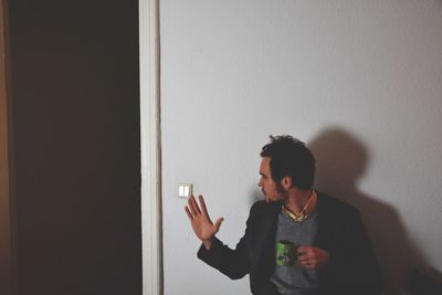 Man gesturing while holding tea cup against wall at home