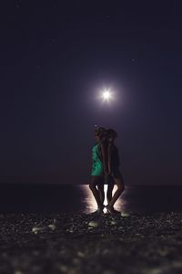 Side view of women standing at beach against sky during night