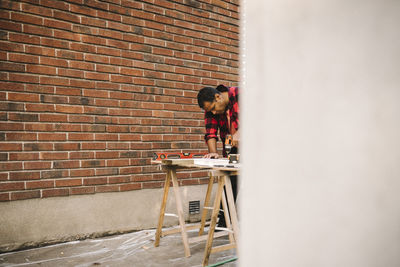 Man using drill machine by brick wall during summer