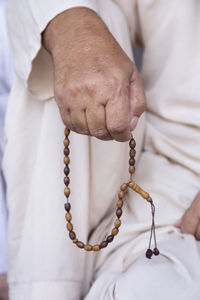 Midsection of man holding bead necklace while praying