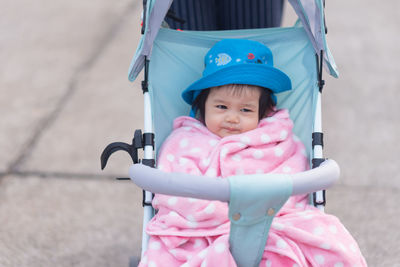 Cute baby wearing hat sitting on baby stroller outdoors